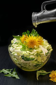 The white cabbage salad in a glass vase on a black background. Low key, decorated with dandelions.