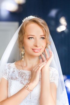 Portrait of beautiful bride with fashion veil posing on bed at wedding morning. Makeup. Brunette girl with long wavy hair styling. Wedding dress.