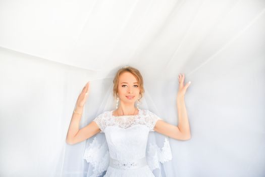 Portrait of beautiful bride with fashion veil posing on bed at wedding morning. Makeup. Brunette girl with long wavy hair styling. Wedding dress.