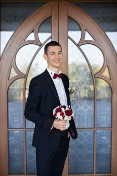 The groom holds a tie and smiles.Portrait of the groom in the park on their wedding day.