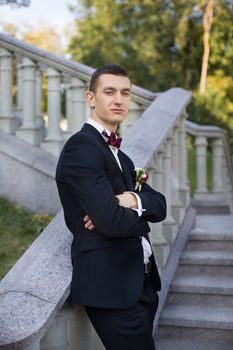 The groom holds a tie and smiles.Portrait of the groom in the park on their wedding day.