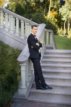 The groom holds a tie and smiles.Portrait of the groom in the park on their wedding day.