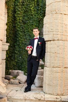 The groom holds a tie and smiles.Portrait of the groom in the park on their wedding day.