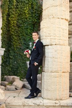 The groom holds a tie and smiles.Portrait of the groom in the park on their wedding day.