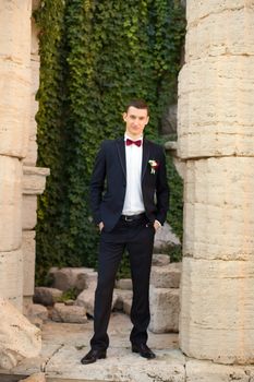 The groom holds a tie and smiles.Portrait of the groom in the park on their wedding day.