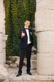 The groom holds a tie and smiles.Portrait of the groom in the park on their wedding day.