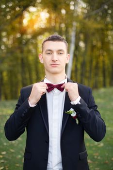 The groom holds a tie and smiles.Portrait of the groom in the park on their wedding day.