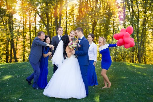 Newlyweds having fun with the guests in a meadow in the park