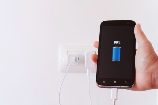 female hand plugging in the wall electtric plug of her smartphone in a socket