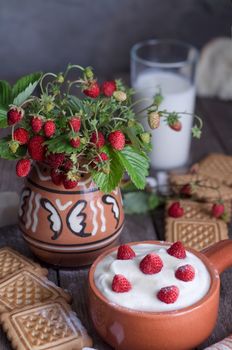 Strawberry with cream in a ceramic Cup, cookies and milk in glass on old wooden surface. Bouquet with strawberries in a ceramic vase. In a rustic style.