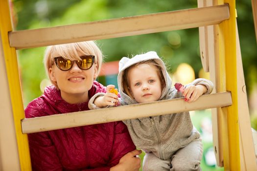 Mother and daughter playing on the playground outdoors on a sunny day