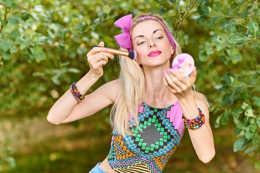 Beauty portrait stylish playful woman smiling primping with mirror, park, people, outdoors. Attractive hipster happy pretty blonde girl with bow, fashionable top. Relax, summer garden, lifestyle,bokeh