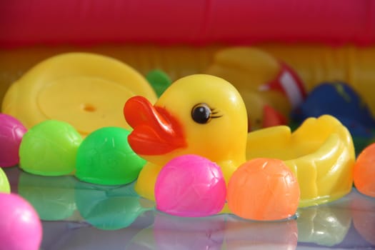 A yellow baby duck toy floating in water along with colorful balls in a baby swimming pool