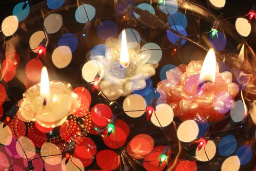 An abstract image of floating candles behind a wire mesh of colorful lights, during Diwali festival in India.