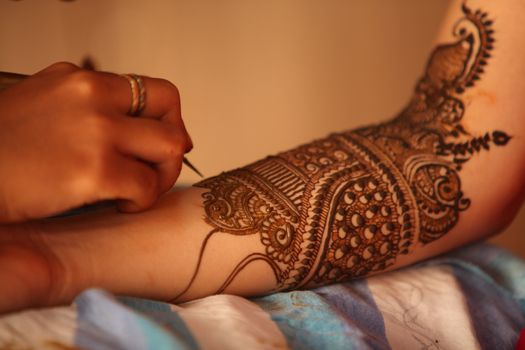 An artist making traditional design with beautiful patterns of henna or mehendi on the hands of an Indian bride.