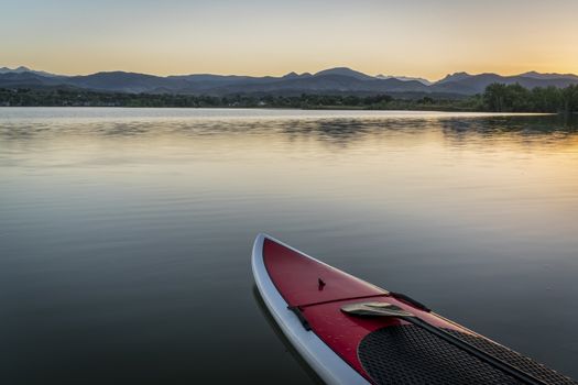 stand up paddleboard with a paddle on calm lake at dusk with Rocky Mountains in background