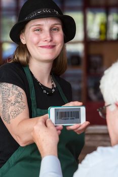 Smiling barista in hat holding smart phone with coupon code for customer