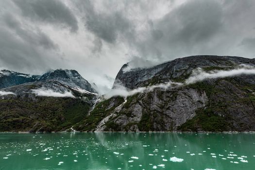 Icy green water of the Endicott Arm Fjord near Juneau in Alaska under dark clouds