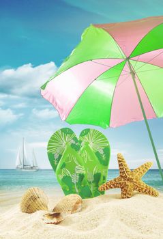 Sandals and seashells with beach umbrella at the ocean