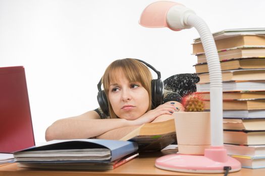 Girl sad student sitting at the table wearing headphones and listening to music