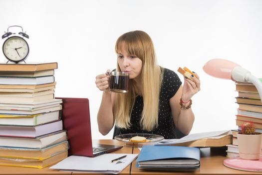 Young teacher drinks coffee with a sandwich in the workplace