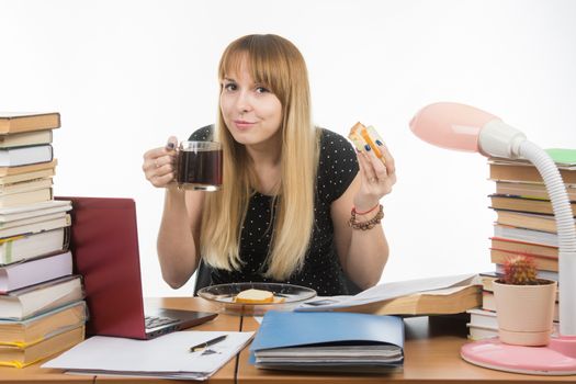 Young teacher drinks coffee with a sandwich in the workplace