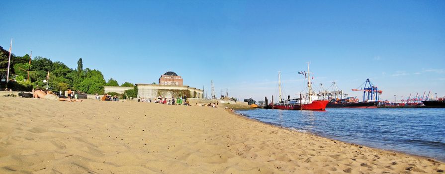 Hamburg, Germany - May 22, 2008: Hamburg city beach panorama (Stadtstrand) in Oevelgonne with sandy beach and harbor with ships and containers on the right.