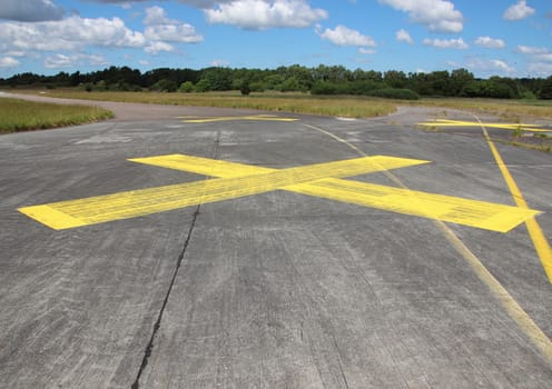 Yellow painted cross on asphalt with clouds in background