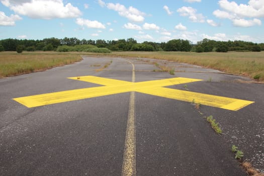 Yellow painted cross on asphalt with clouds in background
