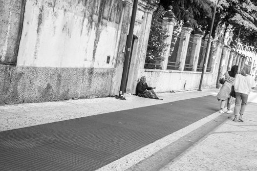 An old woman begging for coins to two woman passing by in the street.