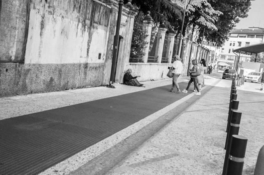 An old woman begging for coins to two woman passing by in the street.