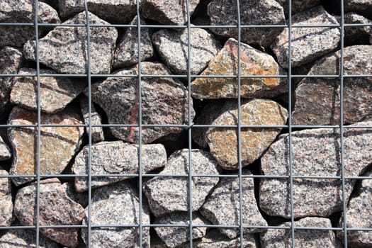 Rocks in solid metal grid wall closeup