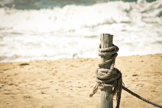 Wooden pole and rope on beach sand waves and sea in the backgrounds