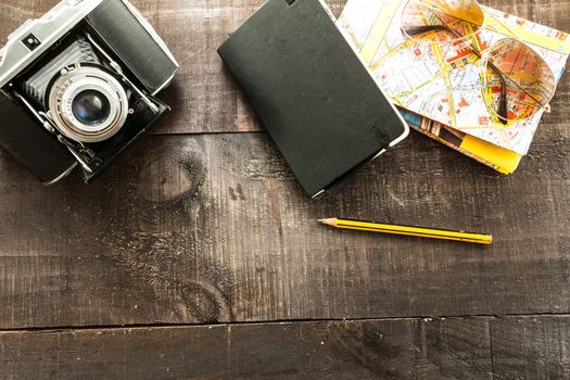 Vintage camera, a map, sunglasses case, polaroid paper an a pencil  on a light wood table