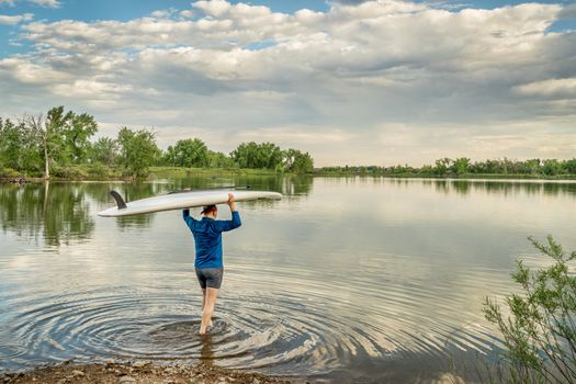 launching stand up paddleboard on a calm  lake in northern Colorado with an early summer scenery