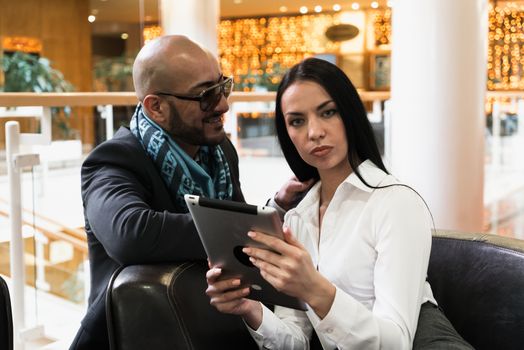 Arab man and stylish girl looking photos on digital tablet in shopping centre