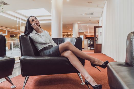 A beautiful girl talking on a smartphone sit on a sofa in the hall of the hotel