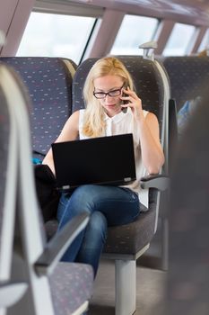 Businesswoman talking on cellphone and working on laptop while traveling by train.