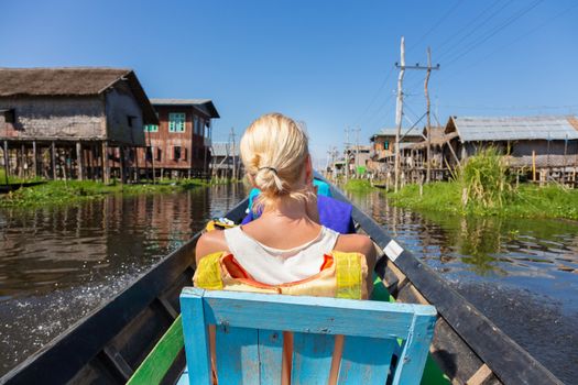 Rear view of female Caucasian tourist traveling by colorful traditional wooden boat on Inle lake, Burma, Myanmar.