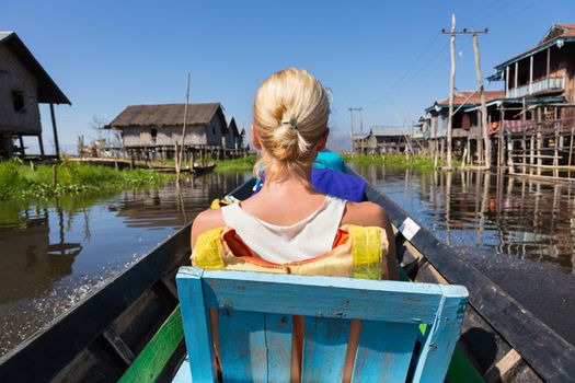 Rear view of female Caucasian tourist traveling by colorful traditional wooden boat on Inle lake, Burma, Myanmar.