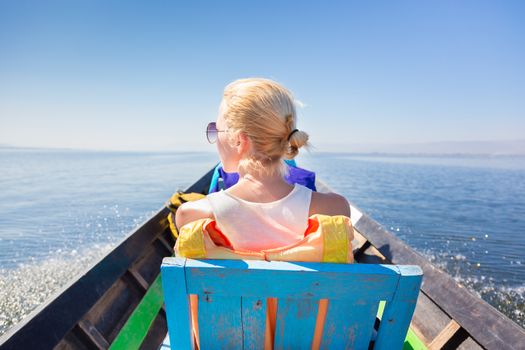 Rear view of female Caucasian tourist traveling by colorful traditional wooden boat on Inle lake, Burma, Myanmar.