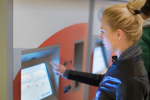 Casually dressed woman, purchasing metro ticket at the ticket vending machine. Urban transport.