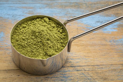 measuring scoop of organic matcha green tea powder against grunge wood