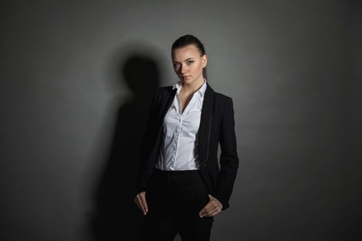 Portrait of young businesswoman in black suit on dark background