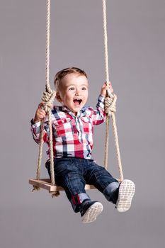 happy little boy swinging on a wooden swing