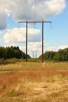 Wooden electrical tower in grass field with clouds