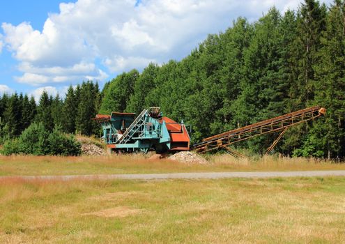 Gravel machine in forest with sky and clouds
