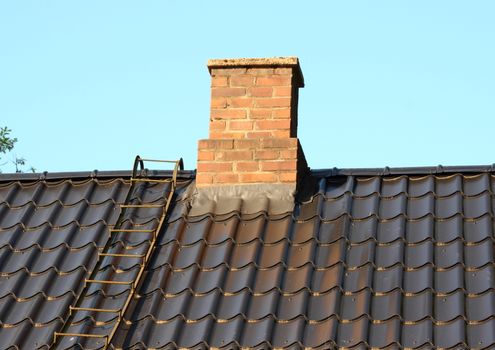 Brick chimney on black roof with metal ladder