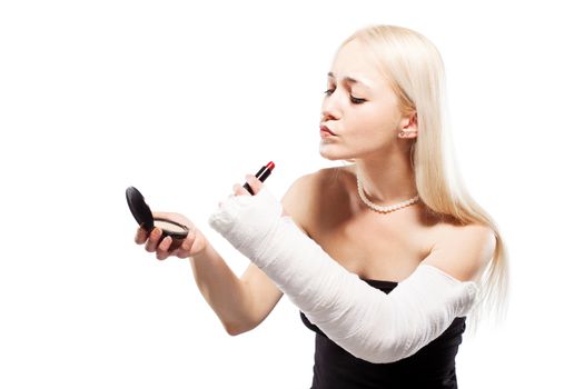 Blond girl with a broken arm in plaster having trouble putting a lipstick