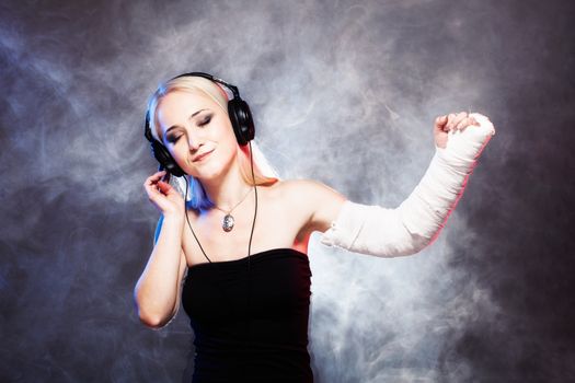 sexy girl with broken arm listening music on headphones and dancing, disco smoke in the background